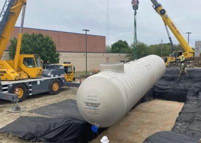 Crane lowering large tank into construction site.