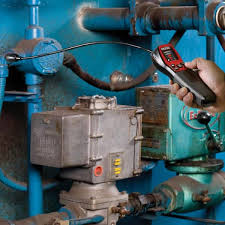Technician using leak detector on industrial equipment.